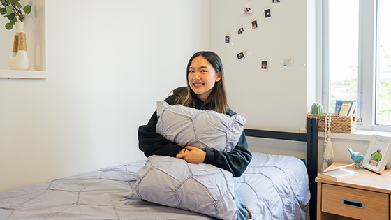 Student sitting on a bed holding a pillow