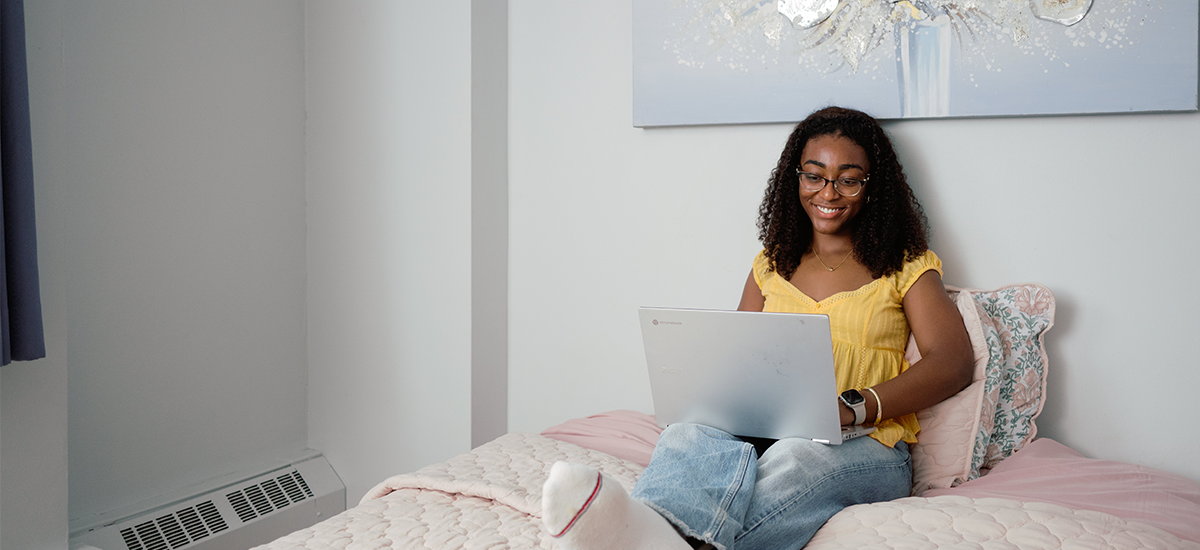 Woman on her bed, doing work on laptop